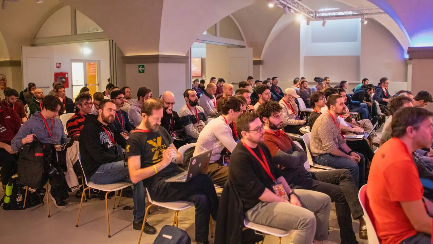 The audience at Open Source Day, rows of people with lanyards watching a talk